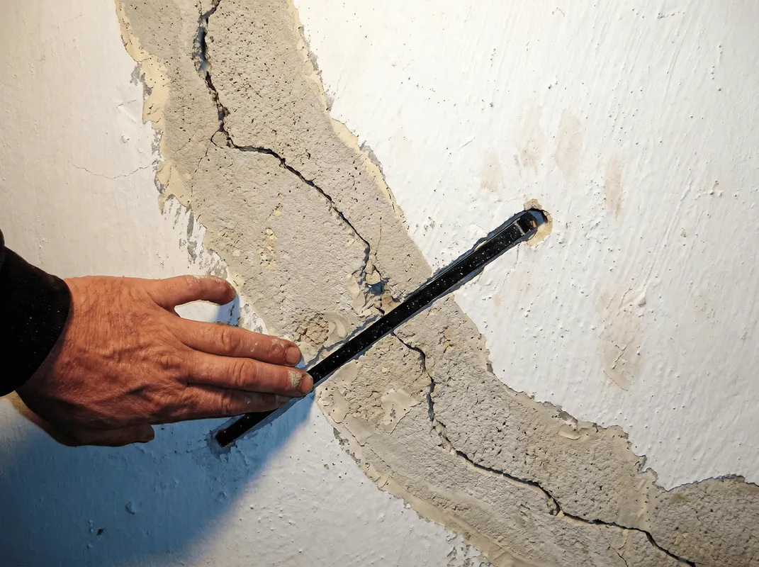 A wall with a large crack is being inspected by a professional in Denver, CO